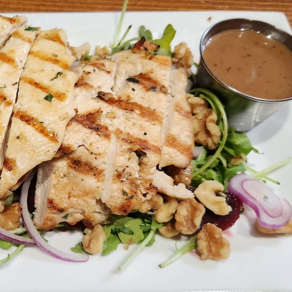 Grilled chicken salad with walnuts, red onion, greens, and a side of dressing.
